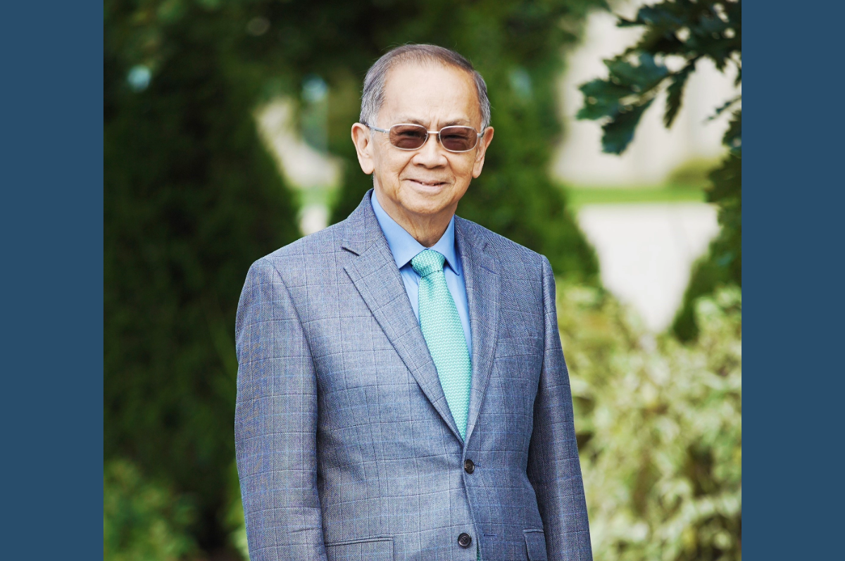 Man in blue jacket standing in front of greenery